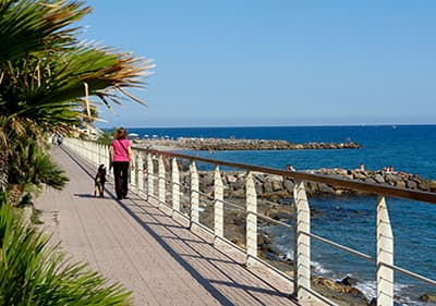 A woman is walking her dog along the coast in Liguria